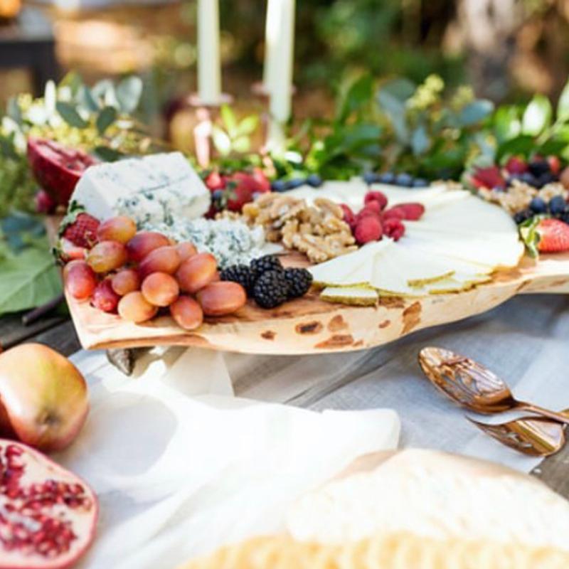 A cheese and fruit board on a live-edge wooden platter — blue cheese, grapes, berries, walnuts and sliced pear — on a candlelit outdoor table.