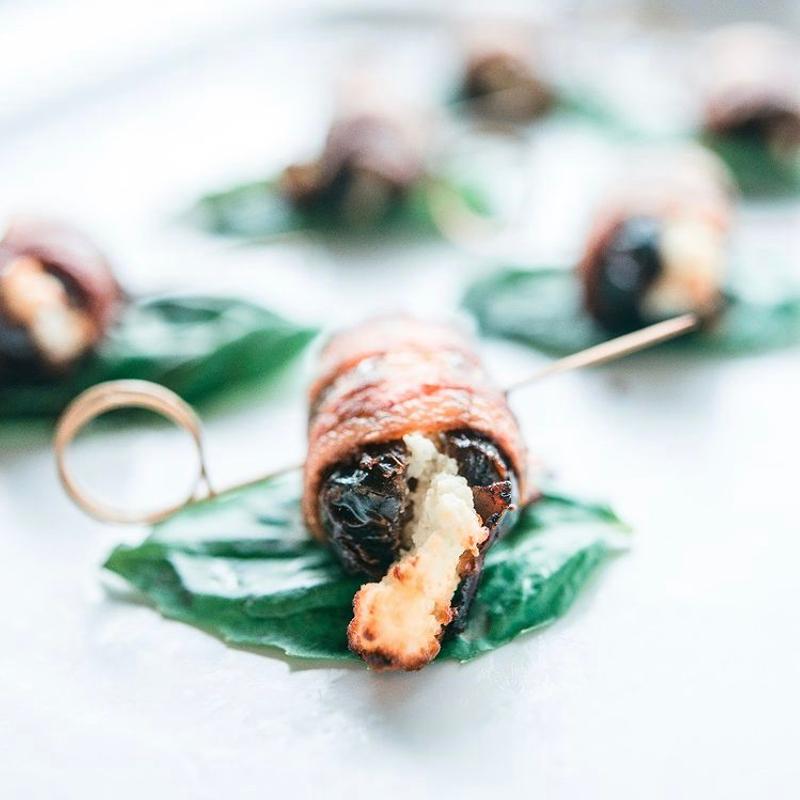 Black pepper bacon wrapped dates stuffed with goat cheese, served on basil leaves with cocktail picks.